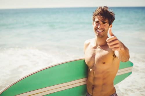 man holding a surfboard giving a thumbs up