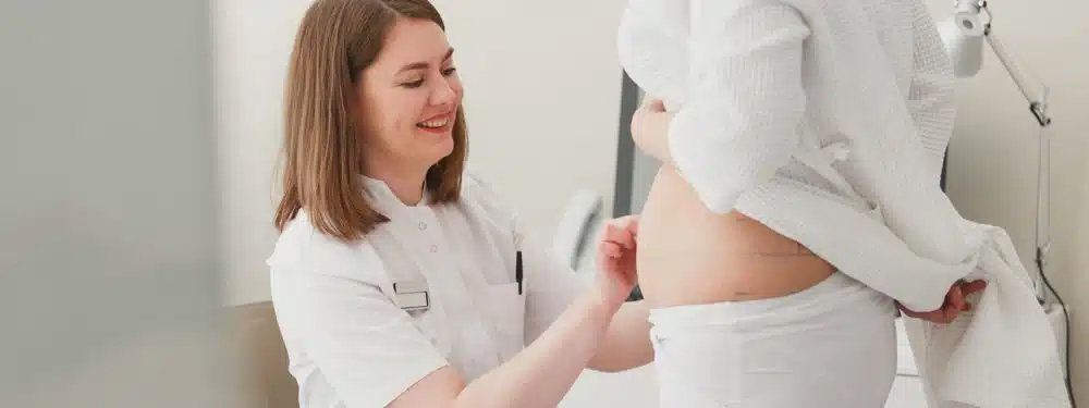 Surgeon taking measurements of the patient's tummy while discussing tummy tucks and weight loss